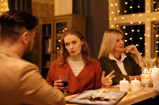 Mulher brava segurando uma taça de vinho e falando com um homem em uma mesa de jantar 