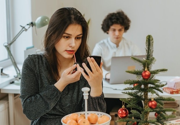 Mulher sozinha se maquiando em uma mesa com comida e uma mini árvore de Natal