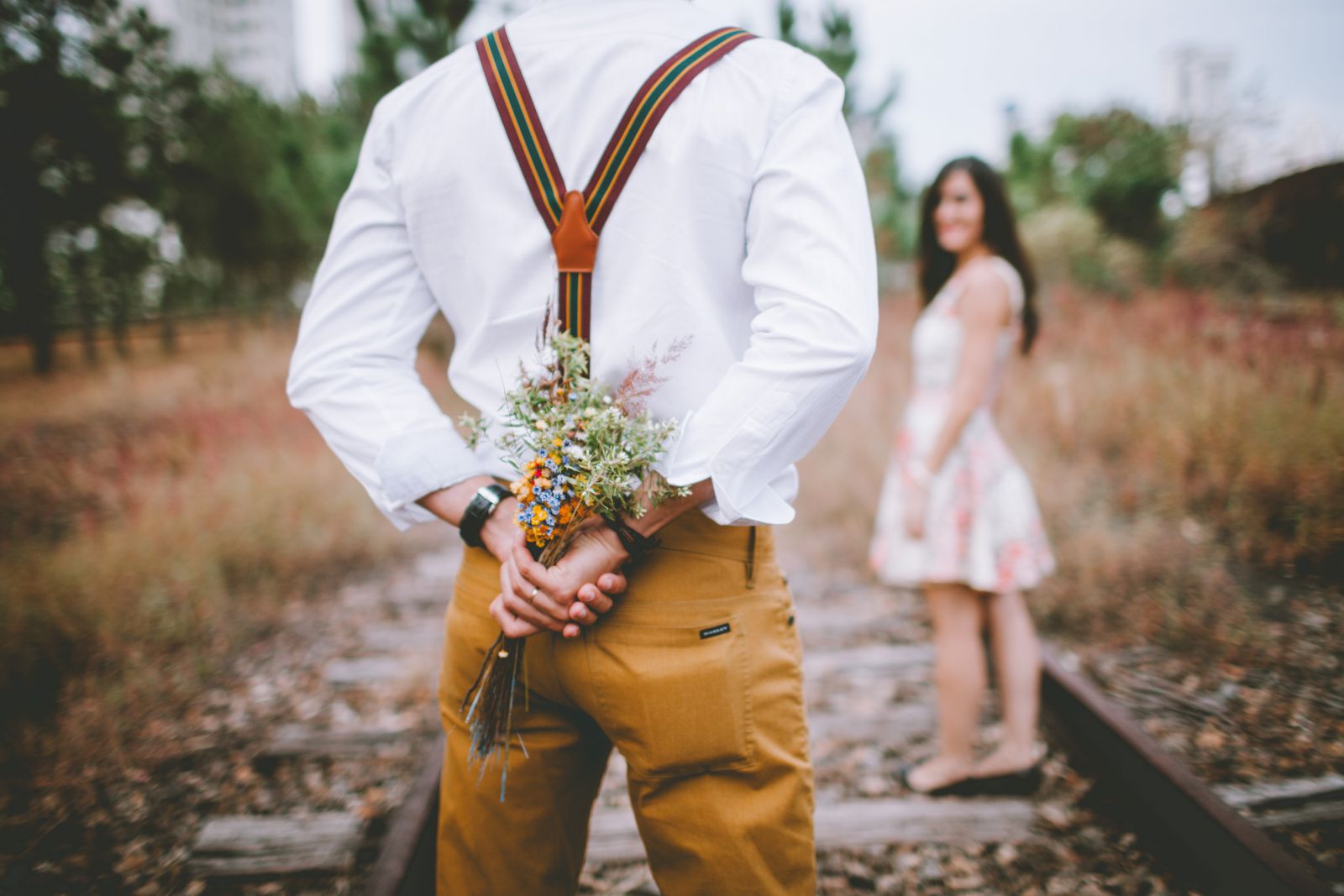 Homem em pé de costas segurando flores com mulher ao fundo