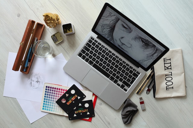 Mesa com notebook e utensílios artísticos.