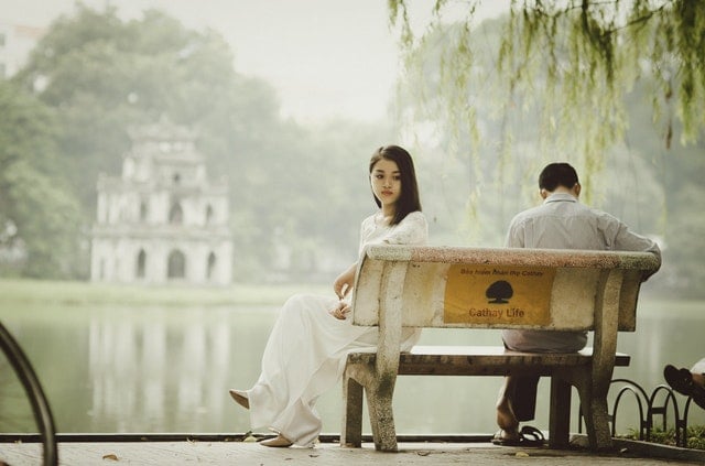 Mulher asiática sentada num banco ao lado de homem.