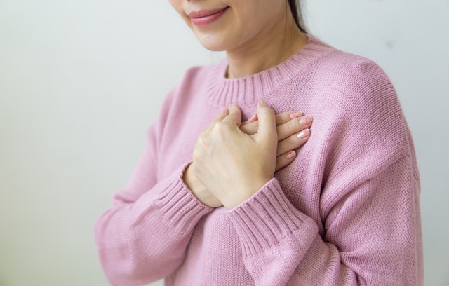 Mulher branca usando suéter rosa com as mãos no coração.