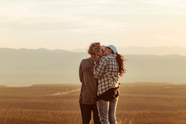 Duas mulheres brancas se beijando num campo.