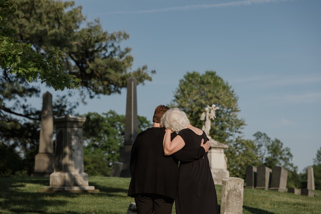 Mulheres brancas se abraçando num cemitério.