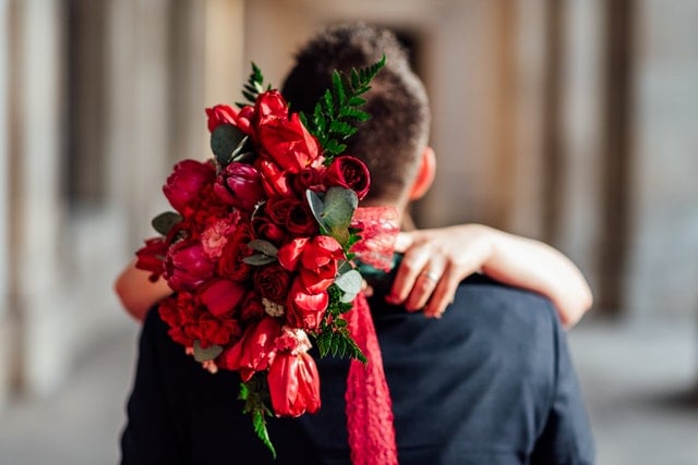 Mulher abraça homem enquanto segura um buquê de flores