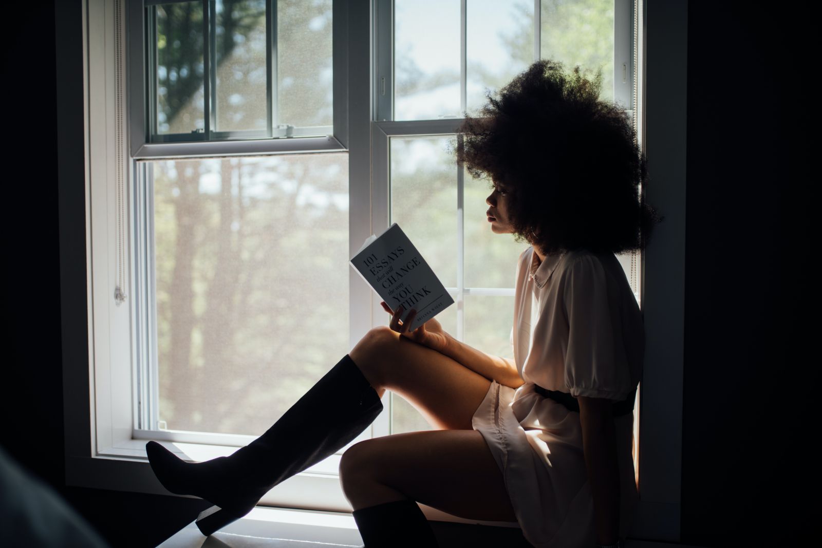 Mulher lendo livro sentada em uma janela