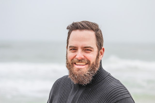 Homem branco com barba grisalha e expressão sorridente.