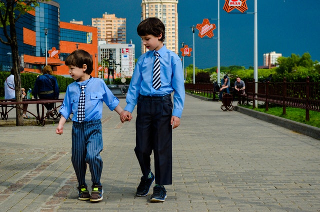 Dois irmãos crianças de roupas sociais caminhando na rua.