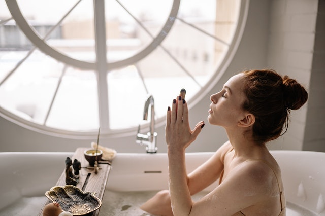 Mulher branca dentro de banheira realizando ritual.