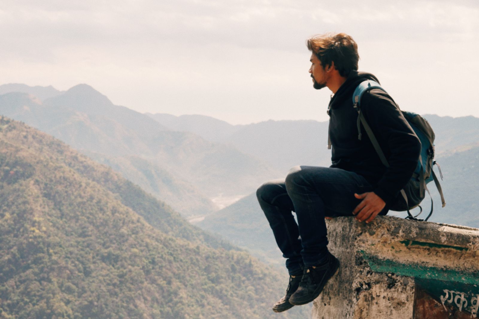 Homem sentado em uma pedra com vista para montanhas