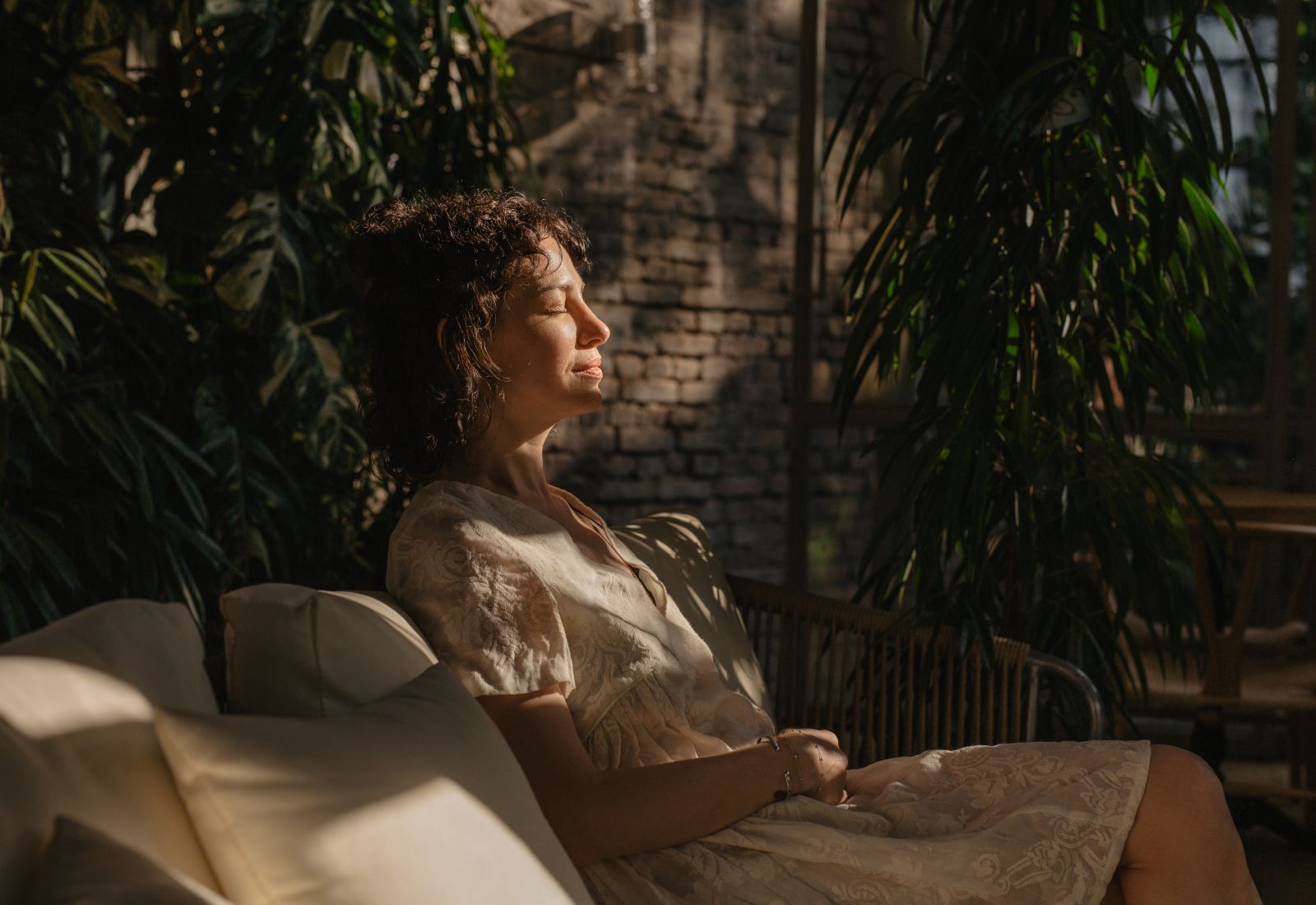 Mulher de olhos fechados sentada em um banco com almofadas