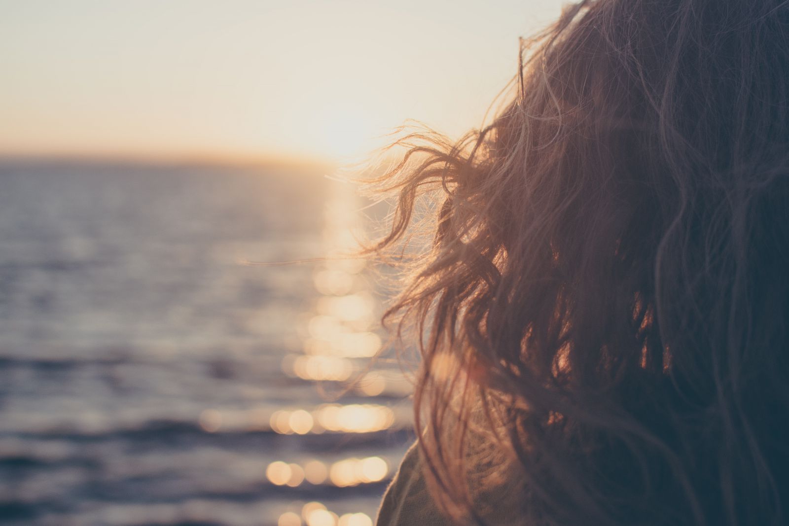Imagem ampliada de uma mulher olhando para o horizonte, em frente ao mar.