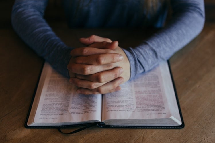 Mãos orando sob uma Bíblia aberta