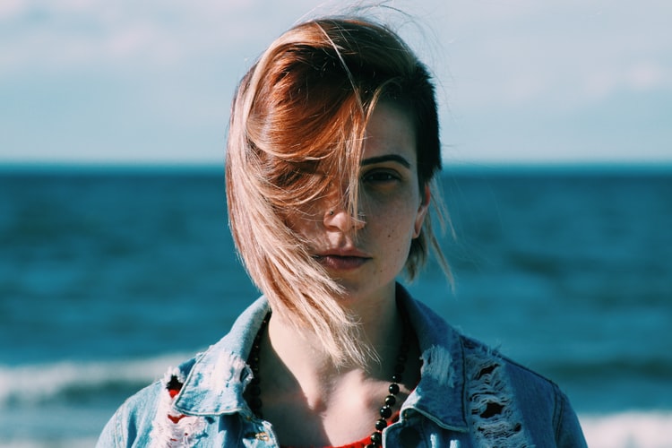 Retrato de uma mulher com os cabelos curtos ao vento em frente ao mar.