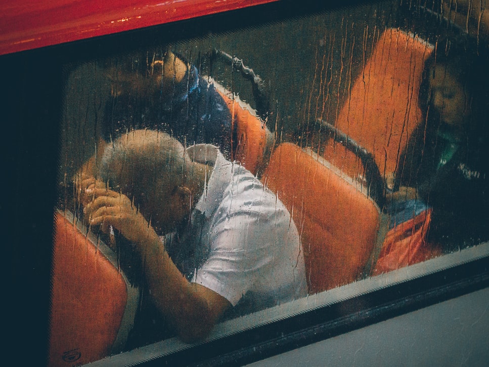 Homem sentado em um ônibus com a cabeça apoiada no banco da frente
