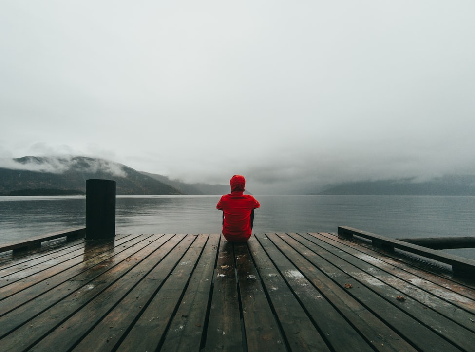 Homem sentado de costas em um deck de madeira observando um lago