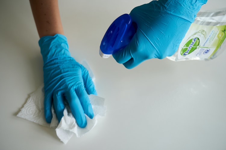 Mãos limpando uma superfície branca com um papel e um produto de limpeza