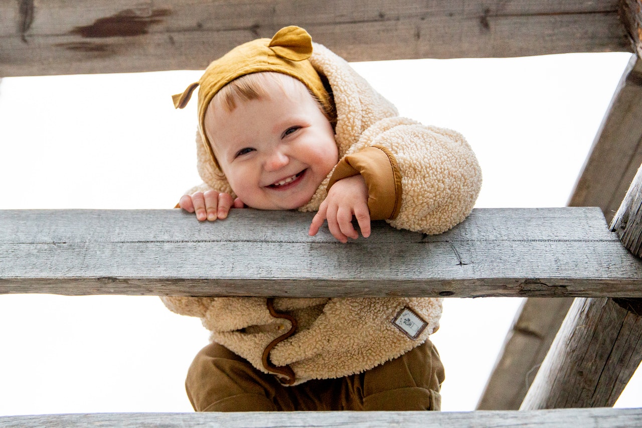 Bebê escalando uma escada de madeira, e sorrindo.