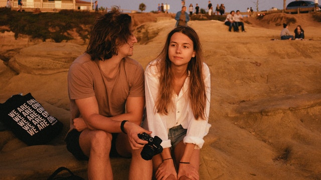 Homem e mulher conversando sentados na areia da praia.