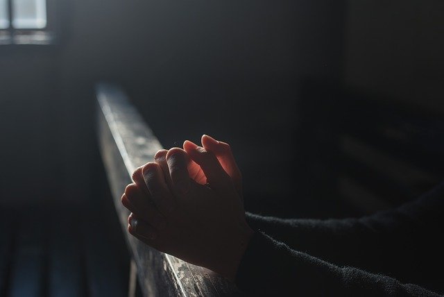 Mãos orando em cima de um banco da igreja