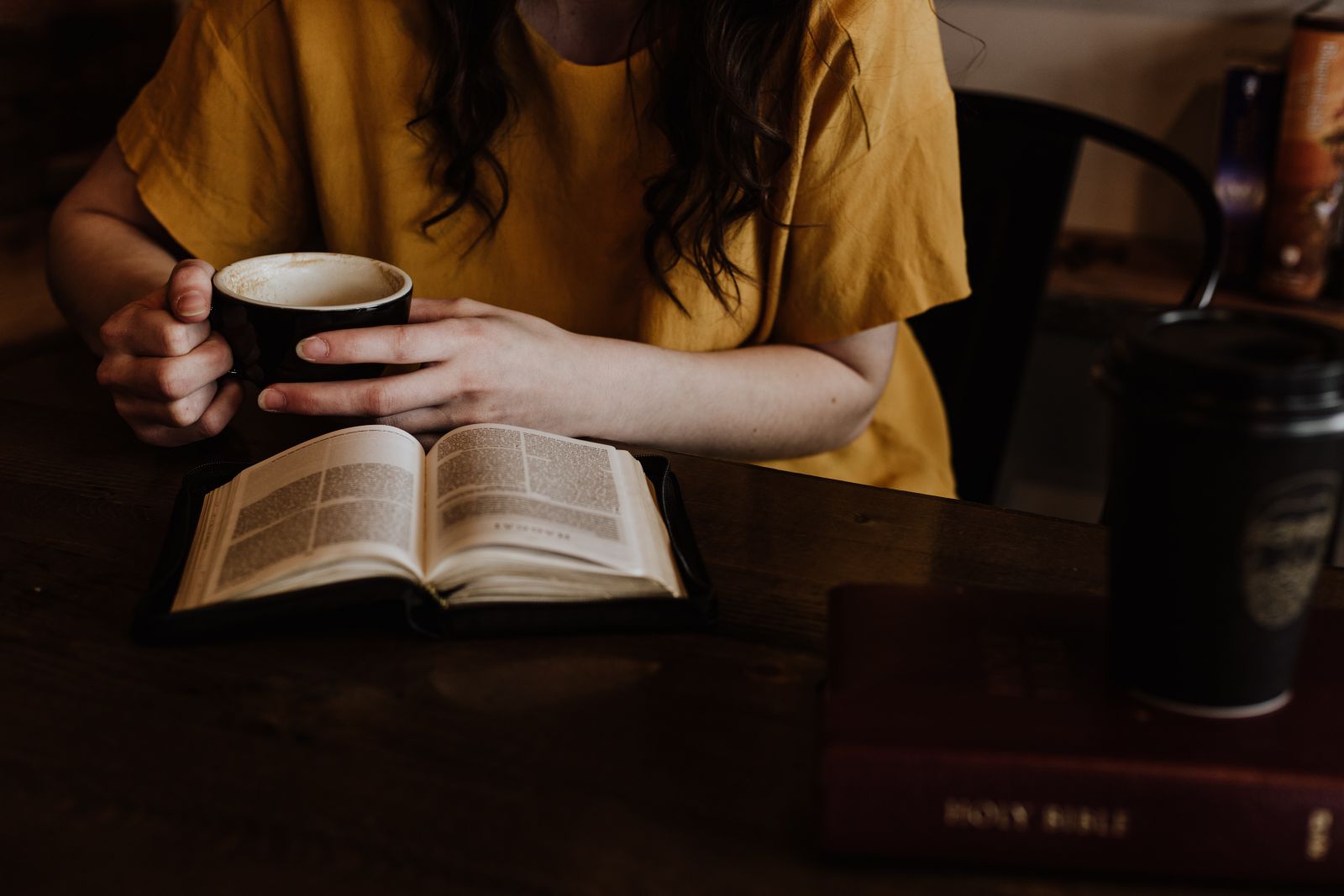 Mulher lendo livro e segurando xícara de café