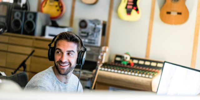 Homem com fones de ouvido sorri. Ele está em um estúdio de música. 