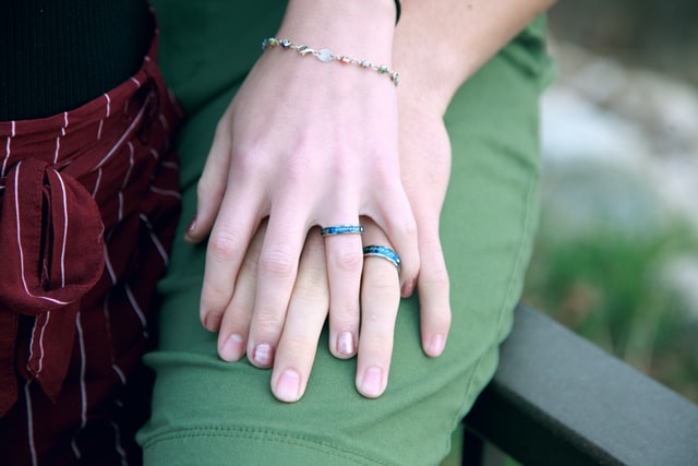 Duas mãos entrelaçadas usando anéis iguais.