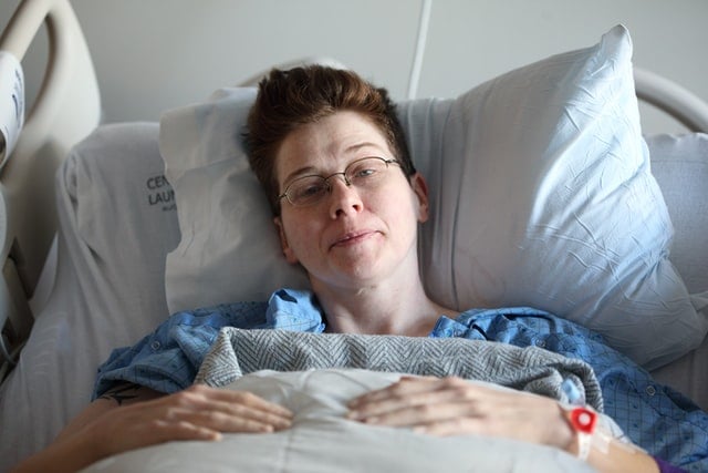 Mulher branca deitada numa cama de hospital.