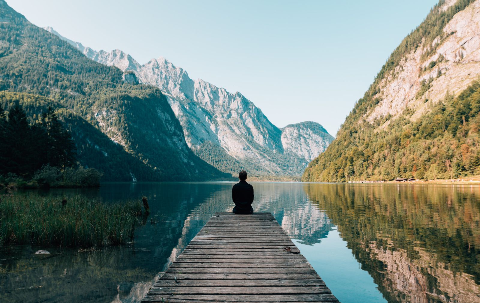 Homem sentado de frente para um lago