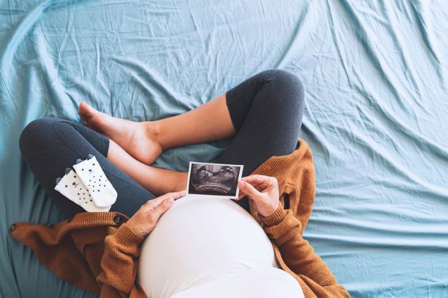 Mulher grávida sentada na cama, segurando uma imagem de ultrassom.