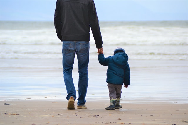 Homem andando de mãos dadas com seu filho pequeno na praia
