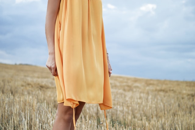 Parte inferior de corpo de mulher branca usando vestido amarelo no campo.