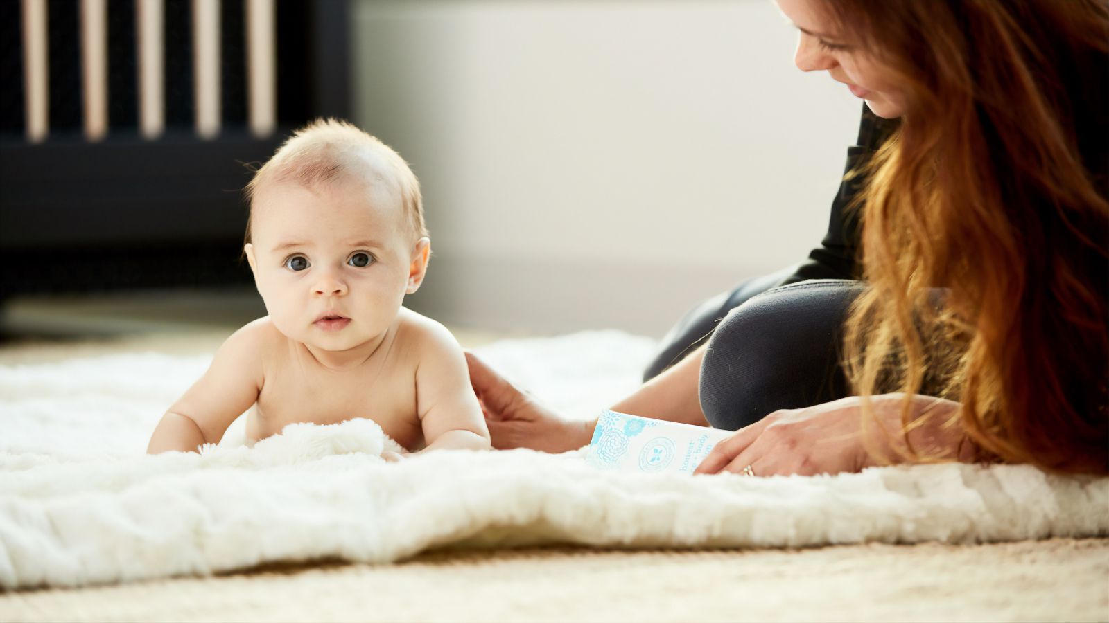 Bebê no chão olhando para frente enquanto mulher está ao seu lado