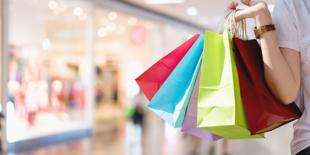 Mulher segura sacolas de compras coloridas em shopping center.