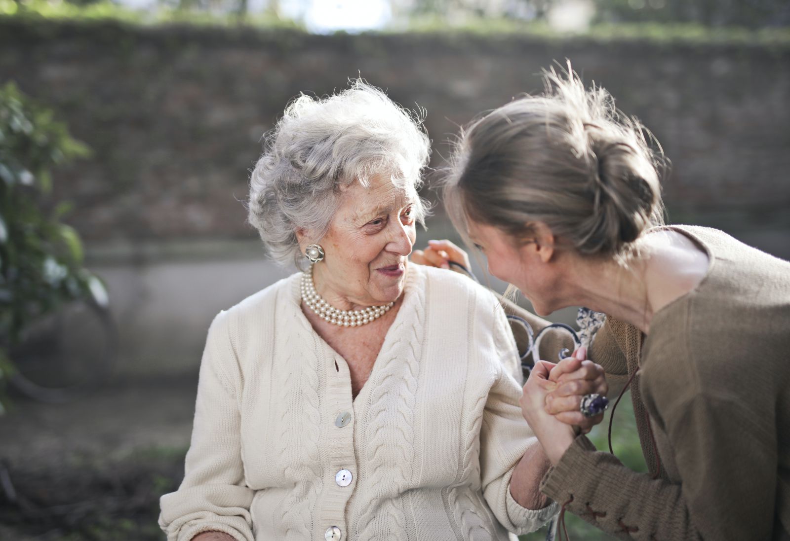 Mulher dando a mão para uma senhora idosa, que está sentada