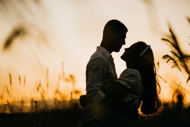 Imagem de um casal se abraçanso em um campo ao pôr-do-sol