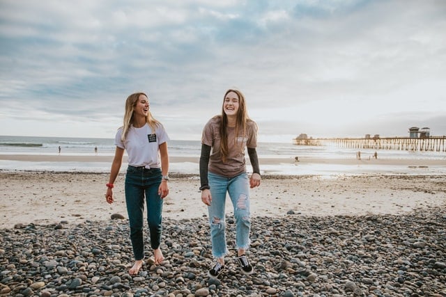 Mulheres brancas caminhando na praia, com expressões sorridentes.