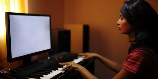 Mulher toca teclado e observa monitor à sua frente.