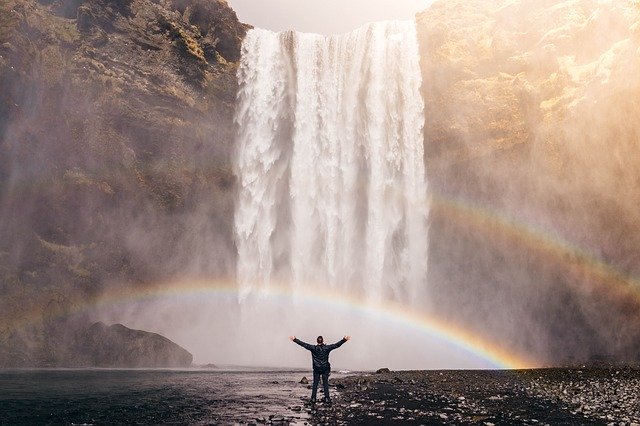 Homem de costas com cachoeira e arco-íris ao fundo