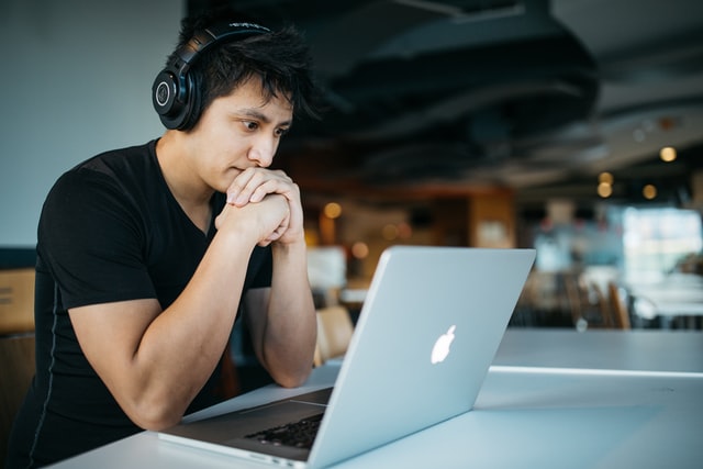 Homem branco sentado em frente à notebook com headphones.