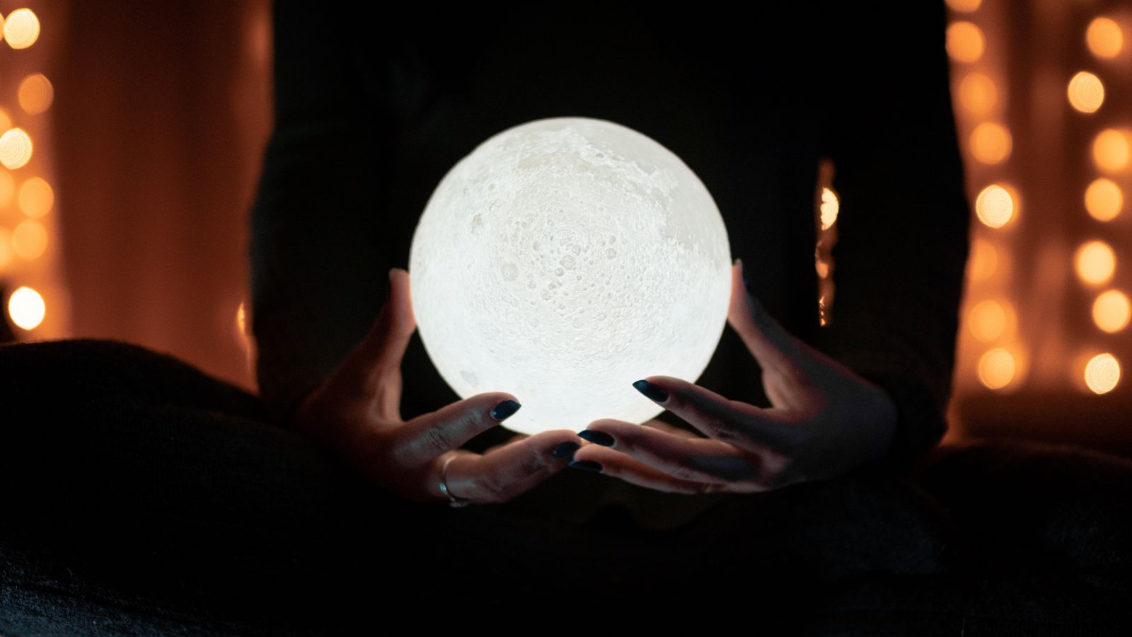 Pessoa segurando uma luminária em formato de lua cheia.