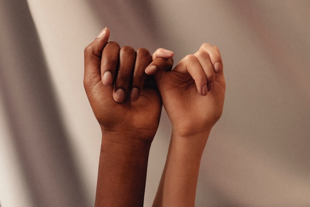 Dedos de mulheres branca e negra entrelaçados.