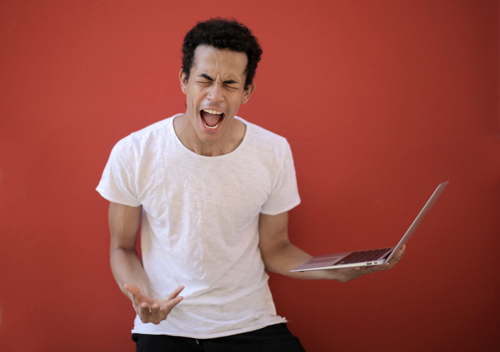 Homem segurando um laptop enquanto grita com expressão de raiva,